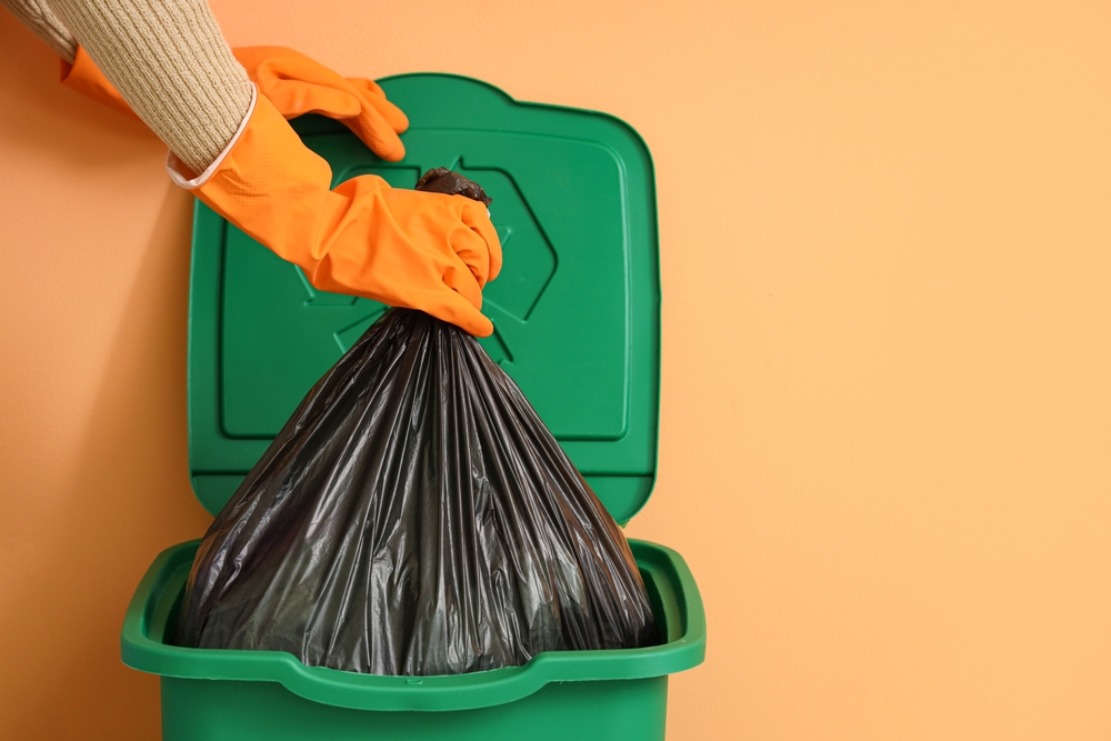 Woman,Taking,Garbage,Bag,From,Trash,Bin,Near,Orange,Wall,